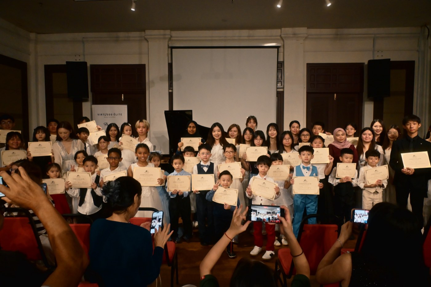 Students and teachers of Virtuoso Élite holding their certificates on stage at the academy's first annual concert