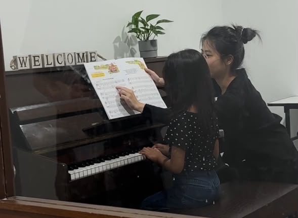 A piano teacher guiding a young student through a score at Virtuoso Élite Music Academy, Kuala Lumpur